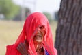 An old indian farmer lady stood up wearing a red Rajasthani veil as per the custom